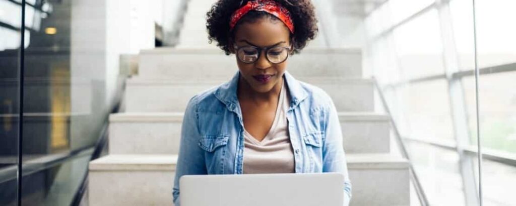 woman sat on steps working on a laptop