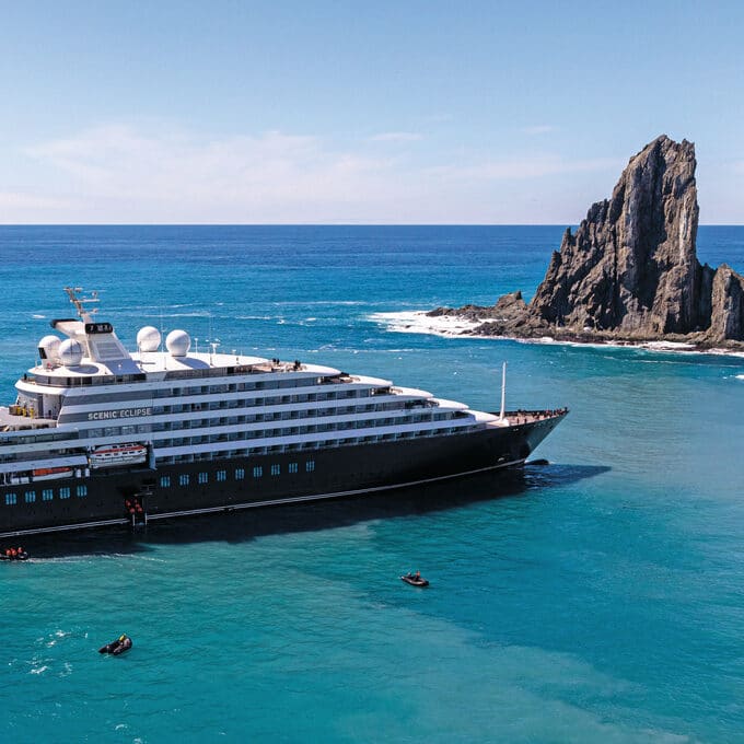 Large black and white cruise ship in a light blue sea with a rock sculpture behind it.