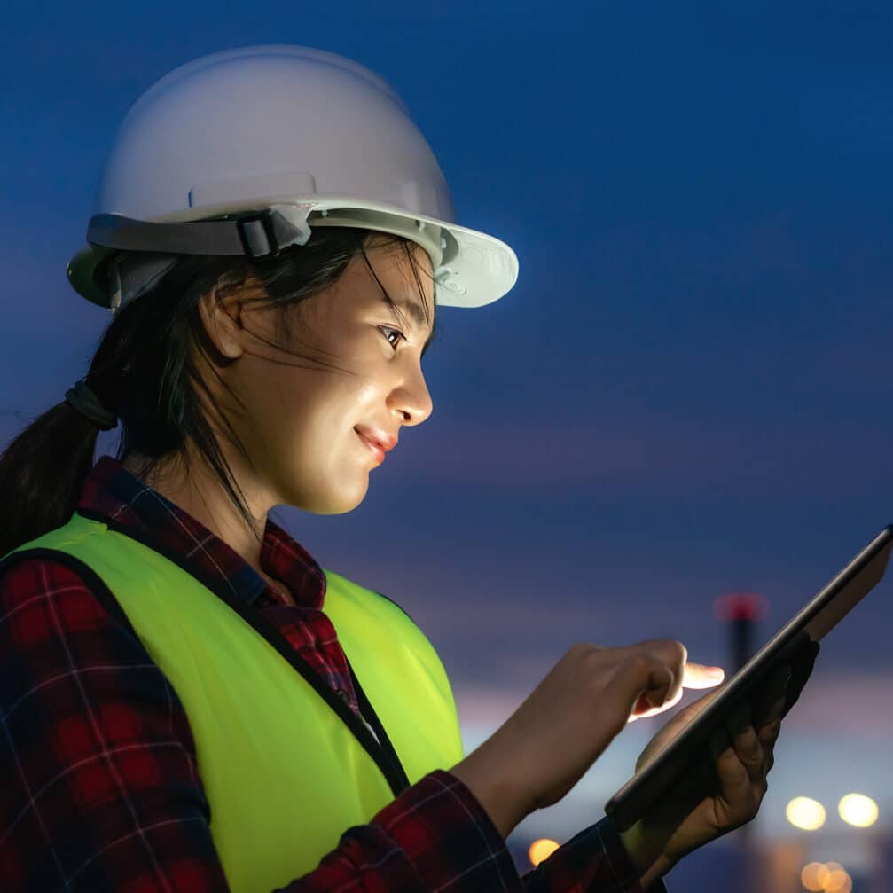 Asian woman, petrochemical engineer working at night with digital tablet Inside oil and gas refinery plant industry factory at night for inspector safety quality control.