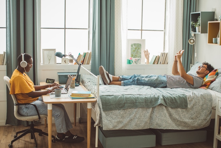 College students at dorm room. Homeschooling. They are studying and using phone.