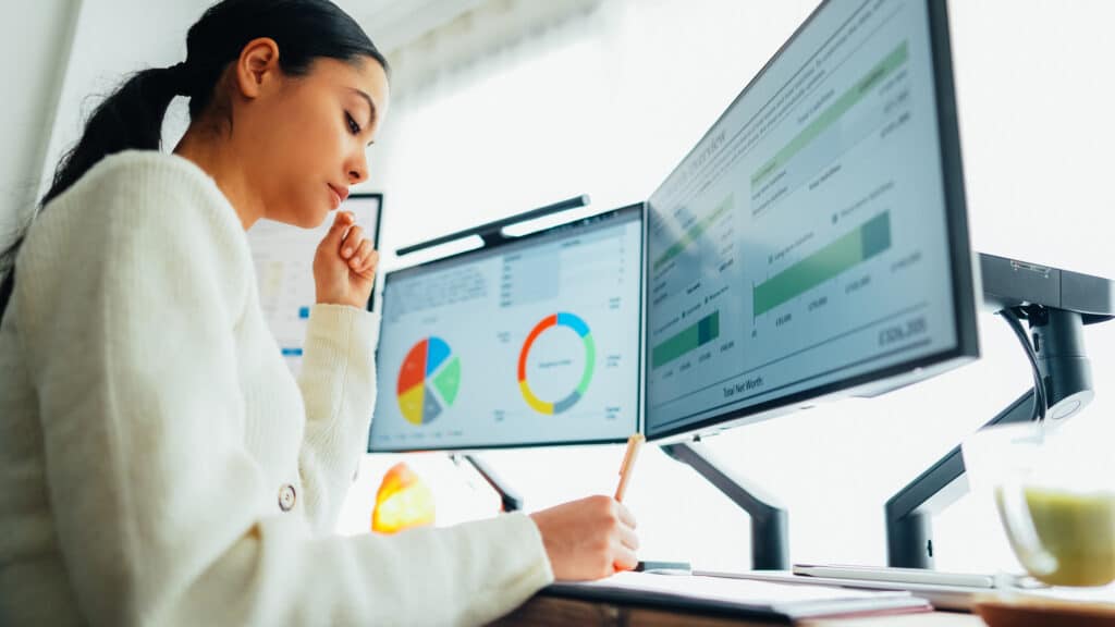 Woman stood at a standing desk in an office, looking at booking data on her computer.