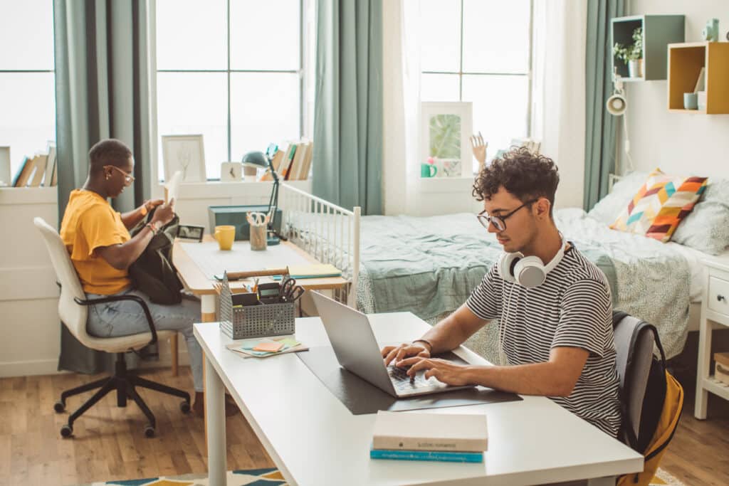 College students at dorm room. Homeschooling. They are studying and using phone.